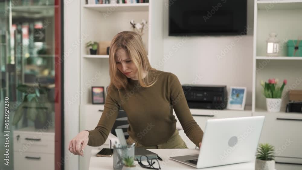 The young woman, blonde, works with a laptop in a modern, bright office. She receives a notification on her phone, and the woman reacts very emotionally and joyfully to the message on her phone The young woman, blonde, works with a laptop in a modern, bright office. She receives a notification on her phone, and the woman reacts very emotionally and joyfully to the message on her phone