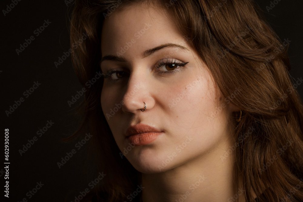 Portrait of a young brunette girl with a haughty look. Close-up, black background. piercing in the nose. Portrait of a young brunette girl with a haughty look. Close-up, black background. piercing in the nose.