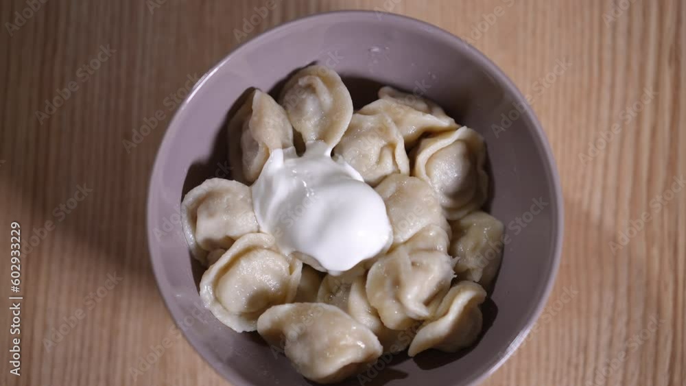 Live camera zoom in to bowl with boiled dumplings and sour cream in slow motion. Top view plate with delicious dinner on table indoors Live camera zoom in to bowl with boiled dumplings and sour cream in slow motion. Top view plate with delicious dinner on table indoors