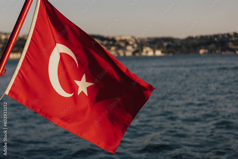 A flag with a city in the backgroundTurkish Flag, Bosphorus and cityscape of Istanbul on the background. Turkish national days concept.