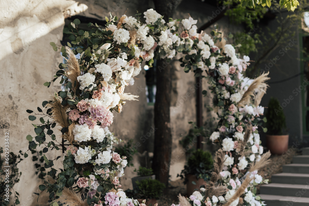 Wedding arch in rustic style decorated with grass hay field colour and flowers. Wedding ceremony in sunny summer day.