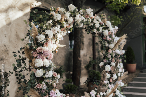 Wedding arch in rustic style decorated with grass hay field colour and flowers. Wedding ceremony in sunny summer day.