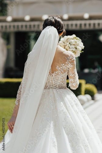 Obraz na płótnie Back view of young bride in a beautiful long classic dress stands with her back with bouquet in hand before the wedding ceremony. Summer wedding. w salonie