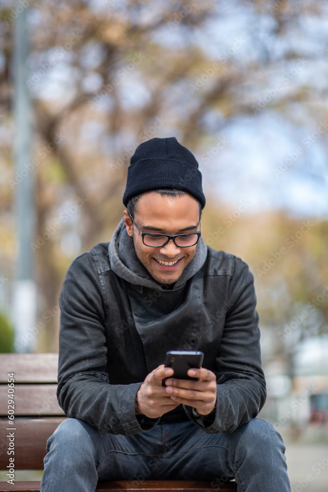 Happy black man using mobile phone while sitting outside Happy black man using mobile phone while sitting outside