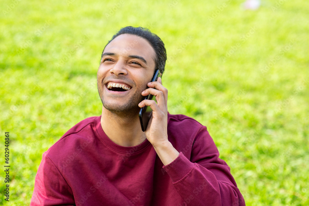 Cheerful young black man sitting in park talking on mobile phone Cheerful young black man sitting in park talking on mobile phone