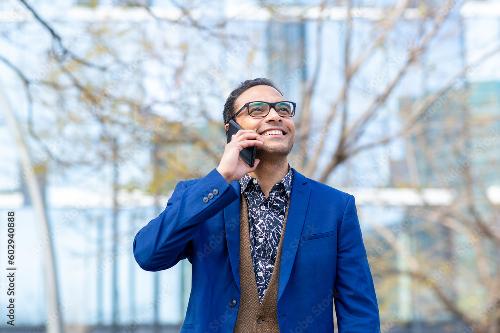 Stylish young businessman talking on cell phone walking outside in city Stylish young businessman talking on cell phone walking outside in city