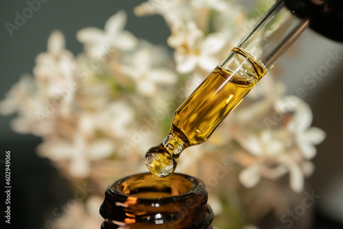 CBD oil drop macro close-up in natural light, organic skincare and wellness concept. White lilac flower on background.