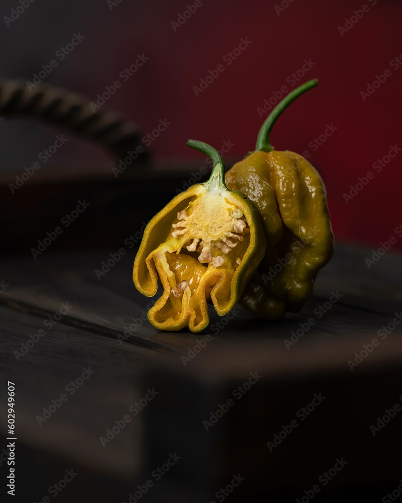 Fototapeta premium Hot mustard pepper habanero. Whole pepper and half stand on wooden surface. Sectional view. Pepper seeds. Spices. Mexican pepper. Spicy food. Close-up. Side view. Soft focus. Copy space.