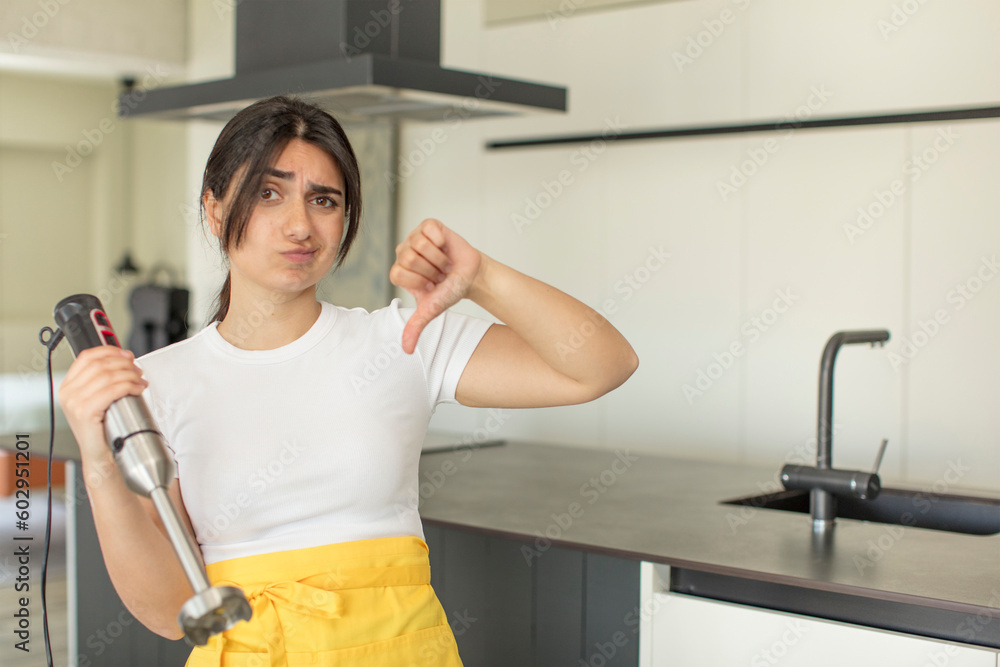 young woman feeling cross,showing thumbs down. chef with hand blender