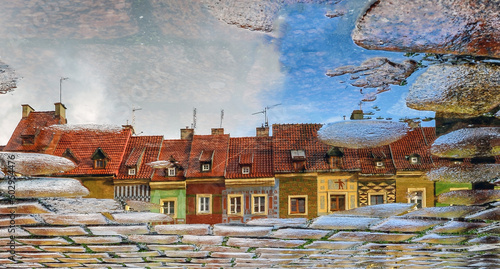 Artistic photo of architecture in Poznań. Buildings in the old market square reflected in a sidewalk puddle. The image is soft and slightly blurred by water.