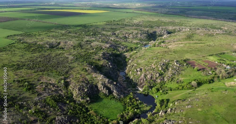 the river flows between large stones in a green field against the background of the sky and clouds. drone view Fields of Ukraine. Actisky canyon the river flows between large stones in a green field against the background of the sky and clouds. drone view Fields of Ukraine. Actisky canyon