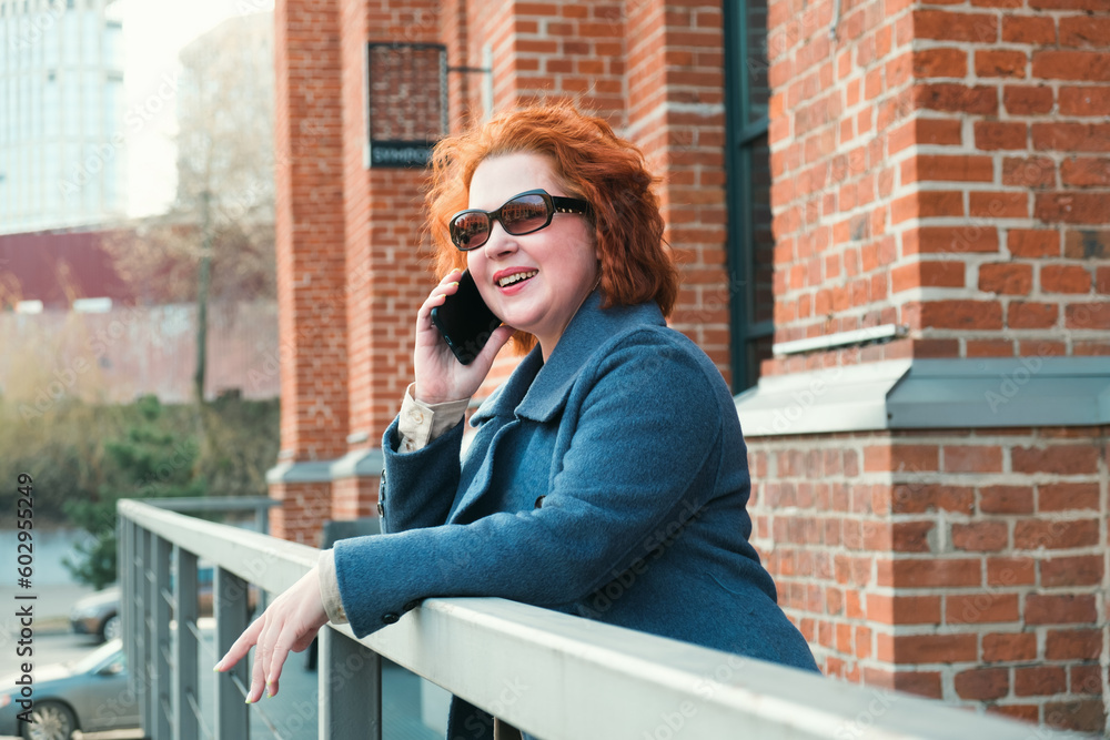 Attractive red-haired woman in a blue coat is talking on a mobile phone. Woman smiling and gesturing emotionally during a telephone conversation.