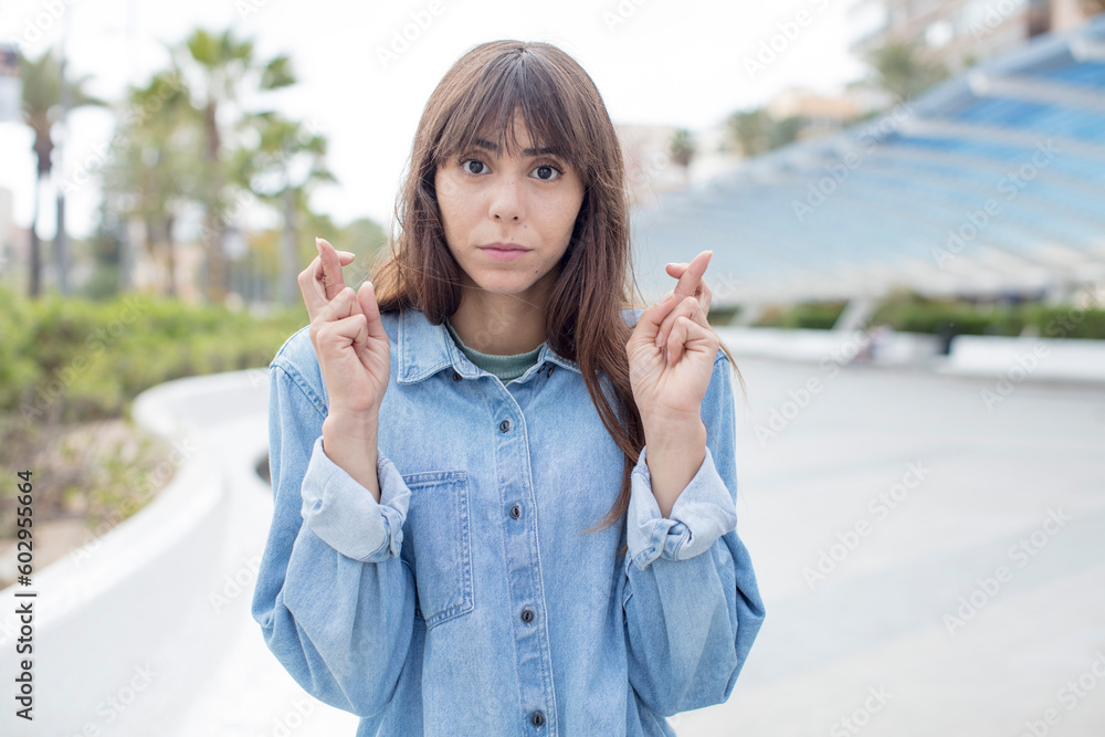 pretty young woman crossing fingers anxiously and hoping for good luck with a worried look