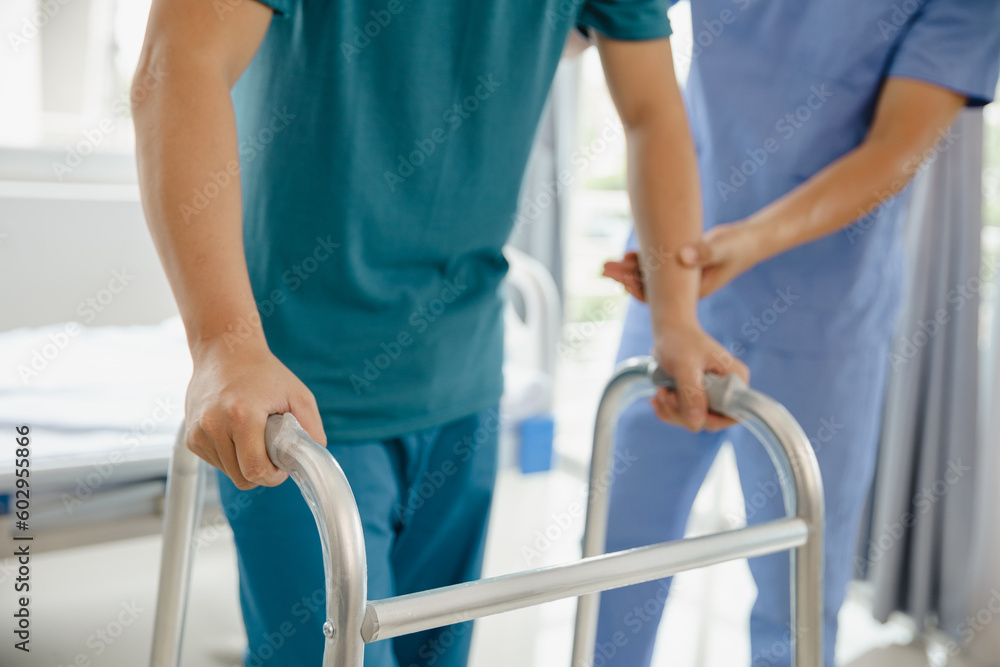 Asian male patient doing physiotherapy with caregiver Attractive specialist caregiver helping and supporting adult man practicing slow walking with walker at nursing home Asian male patient doing physiotherapy with caregiver Attractive specialist caregiver helping and supporting adult man practicing slow walking with walker at nursing home