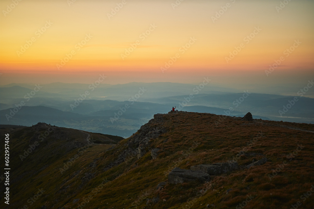 Man looking at sunrise. Mountains at sunrise. Man standing on peak. Natural mountain landscape with illuminated misty peaks, foggy slopes and valleys