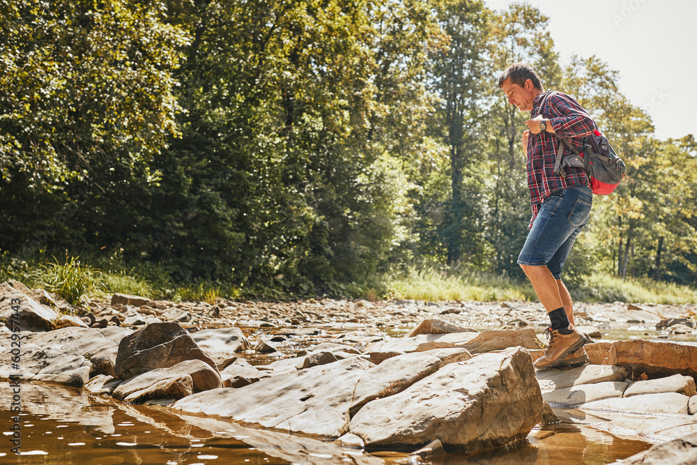 Trekking with backpack concept image. Backpacker wearing trekking boots crossing mountain river. Man hiking in mountains during summer trip Trekking with backpack concept image. Backpacker wearing trekking boots crossing mountain river. Man hiking in mountains during summer trip