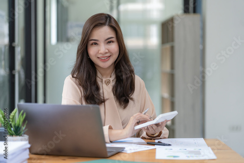 Asian businesswoman looking at camera holding a calculator at the office.