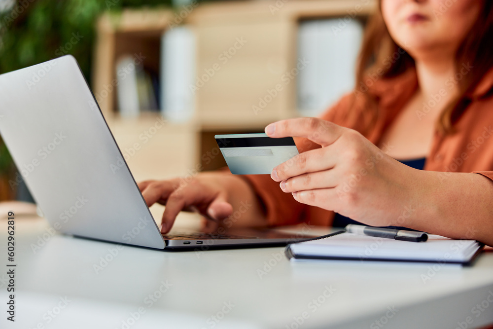 A plus-size woman typing on a laptop and using a credit card for some online shopping. A plus-size woman typing on a laptop and using a credit card for some online shopping.