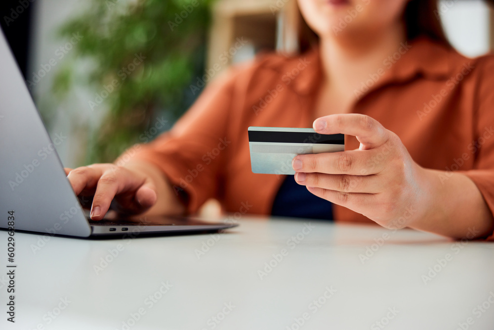 A close-up of a woman holding a credit card and shopping online over the laptop.