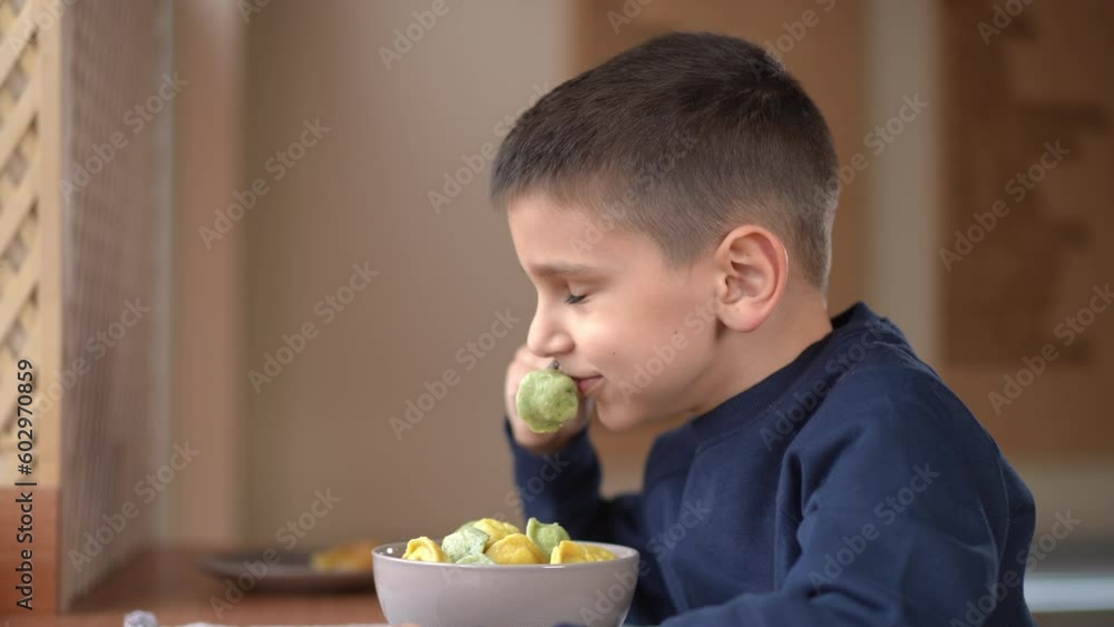 Side view portrait of happy boy smelling hot tasty dumpling in slow motion. Smiling Caucasian kid enjoying dinner sitting at table in cafe indoors Side view portrait of happy boy smelling hot tasty dumpling in slow motion. Smiling Caucasian kid enjoying dinner sitting at table in cafe indoors