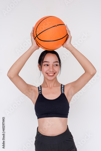 A sporty and athletic young woman posing while holding up a basketball above the head with both hands. Isolated on a white background.