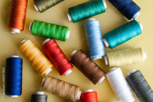 Many spools of sewing thread with assorted colors on a yellow background.
