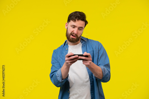 Portrait of an excited young man playing games on mobile phone isolated over yellow background © kinomaster
