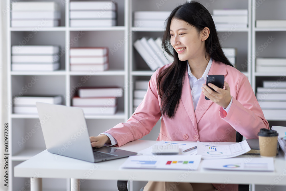 Young Asian professional business woman office worker analyst sitting at desk call phone laptop thinking on project plan, analyzing marketing or financial data online, watching elearning webinar. Young Asian professional business woman office worker analyst sitting at desk call phone laptop thinking on project plan, analyzing marketing or financial data online, watching elearning webinar.