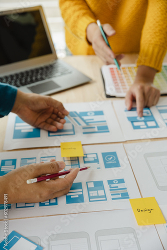 Close up ux developer and ui designer brainstorming about mobile app interface wireframe design on table with customer breif and color code at modern office.Creative digital development agency