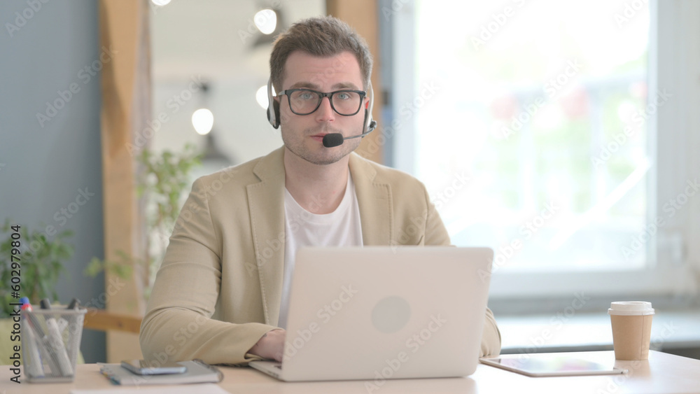 Young Businessman with Headset Looking toward Camera in Call Center Young Businessman with Headset Looking toward Camera in Call Center
