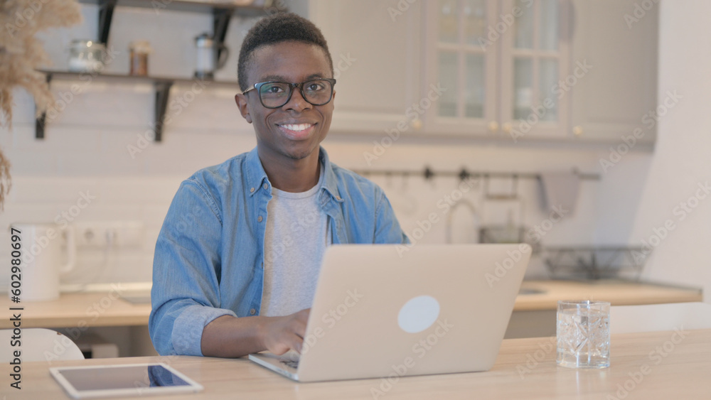 Young African Man Smiling at Camera while Working on Laptop Young African Man Smiling at Camera while Working on Laptop