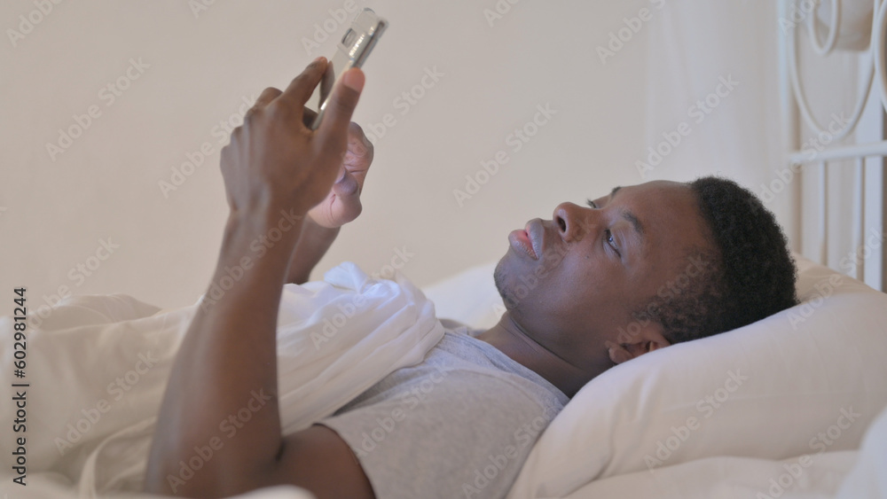 Obraz premium Side View of Young African Man using Phone in Bed