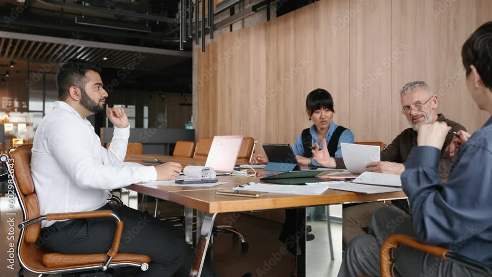 Serious multinational team of colleagues gathered around table discussing project in office Serious multinational team of colleagues gathered around table discussing project in office