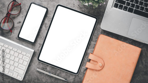 Dark office desk workplace with blank screen tablet and smartphone, laptop, keyboard, pen, eyeglass and notebook, Top view flat lay.