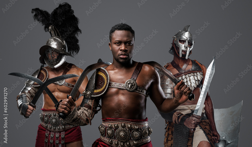 Portrait of handsome african gladiator from past with paired swords and two comrades.