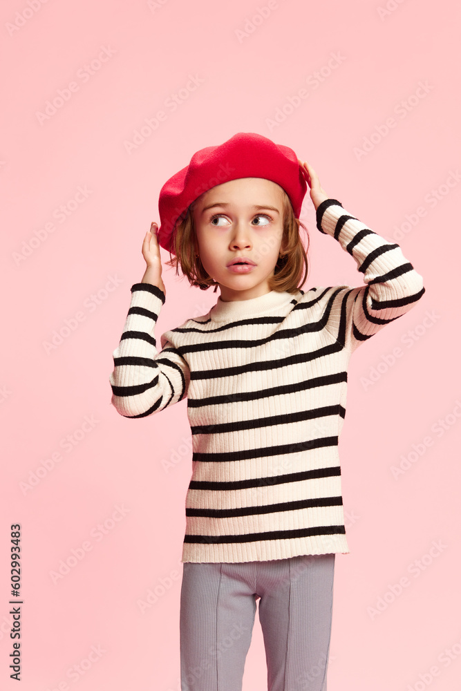 Portrait of beautiful, stylish little girl, child in red beret and striped sweater against pink studio background. Parisian style. Concept of childhood, emotions, fun, fashion, lifestyle Portrait of beautiful, stylish little girl, child in red beret and striped sweater against pink studio background. Parisian style. Concept of childhood, emotions, fun, fashion, lifestyle