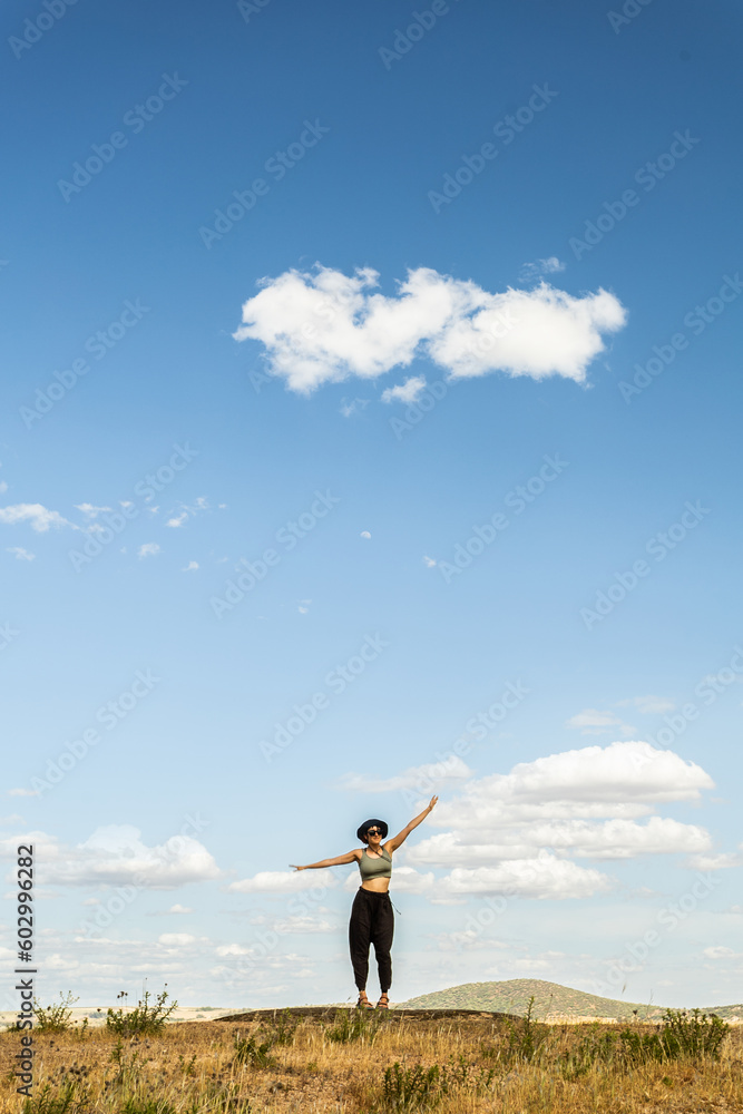 red-haired woman with outstretched arms in a meadow with white clouds and blue sky in the background red-haired woman with outstretched arms in a meadow with white clouds and blue sky in the background