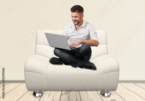 Joyful young man sitting in armchair, with modern laptop © BillionPhotos.com