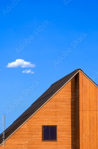 Glass attic window on wooden gable roof of vintage house against blue sky in minimal style and vertical frame