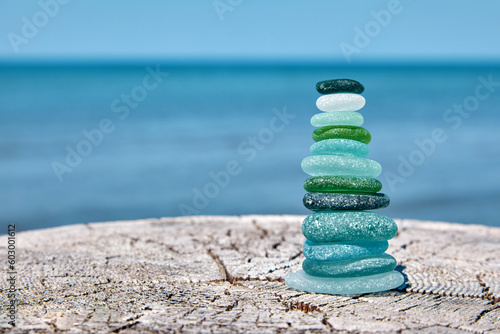 Fototapeta Naklejka Na Ścianę i Meble -  Balanced pyramid of sea-polished glass bottle shards on a weathered wooden surface against the backdrop of the sea