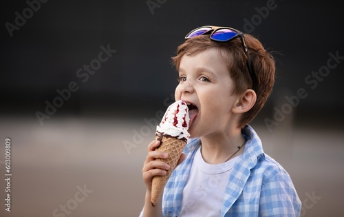 Cute boy 7 years old keeps eating ice cream outdoors in summer

