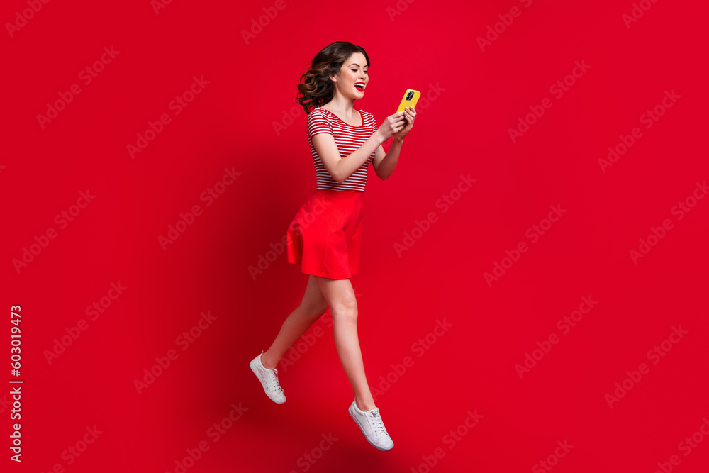 Full length photo of positive lady wear stylish clothes use modern device hurry shop sale walk empty space isolated red color background