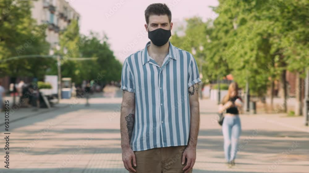 Time lapse portrait of good-looking man wearing medical mask standing alone in crowded city street. Covid-19 pandemic and people concept.