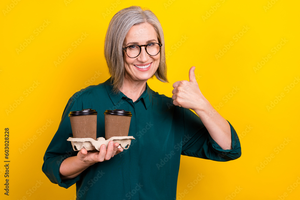 Portrait of attractive lady hold coffee cup order show thumb up wear green isolated on yellow color background Portrait of attractive lady hold coffee cup order show thumb up wear green isolated on yellow color background