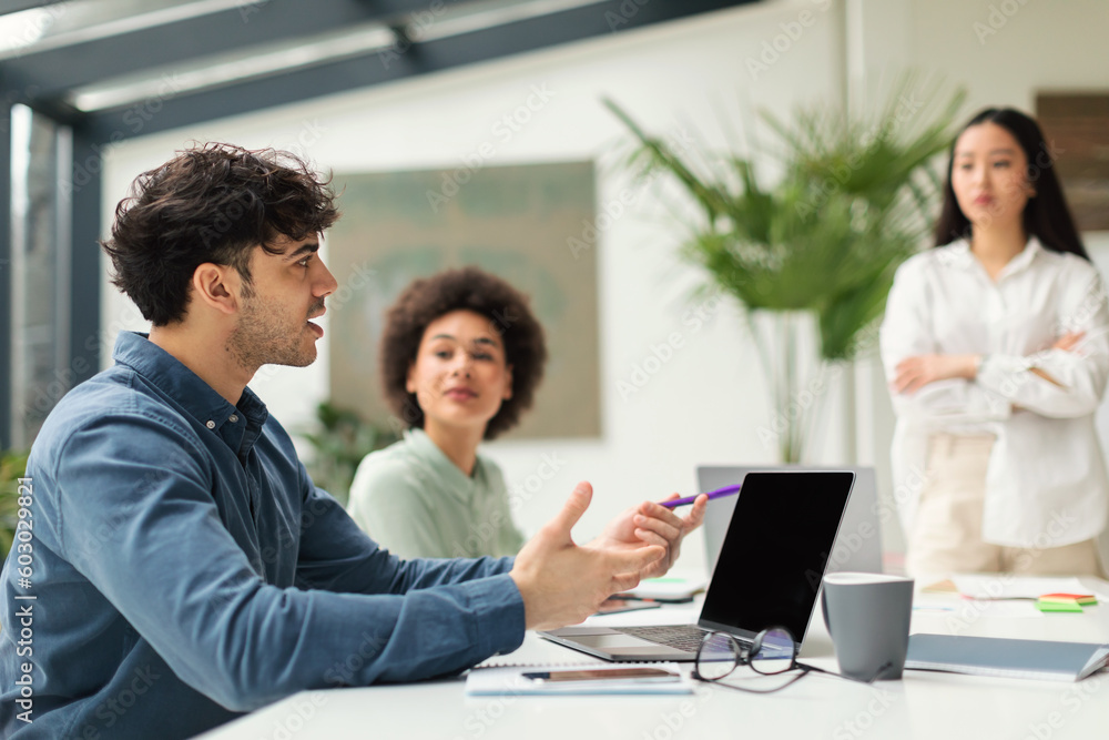 Arabic Guy At Laptop Talking To Colleagues Women In Office Arabic Guy At Laptop Talking To Colleagues Women In Office