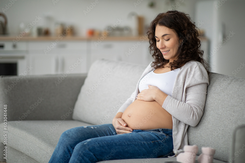 Pregant woman caressing her baby bump while relaxing on couch at home Pregant woman caressing her baby bump while relaxing on couch at home