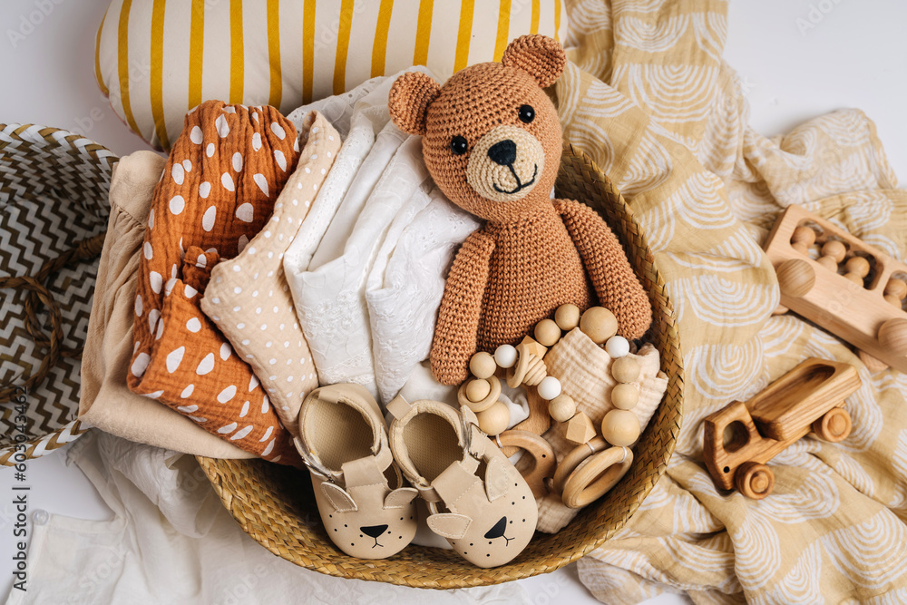 Basket with baby stuff and accessories for newborn. Gift basket with cotton clothes and muslin swaddle blanket, baby shoes, toys and cute teddy bear in beige colors. - obrazy, fototapety, plakaty 