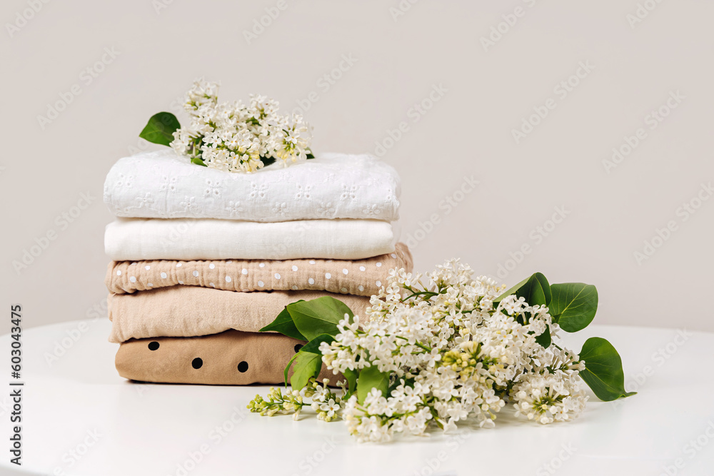 Stack of baby clothes with flowers. Cotton clothes and muslin swaddle blanket in pastel colors. Clean freshly laundered, neatly folded kids clothes. - obrazy, fototapety, plakaty 