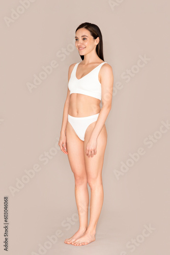Full length of cheerful slender lady wearing underwear on beige