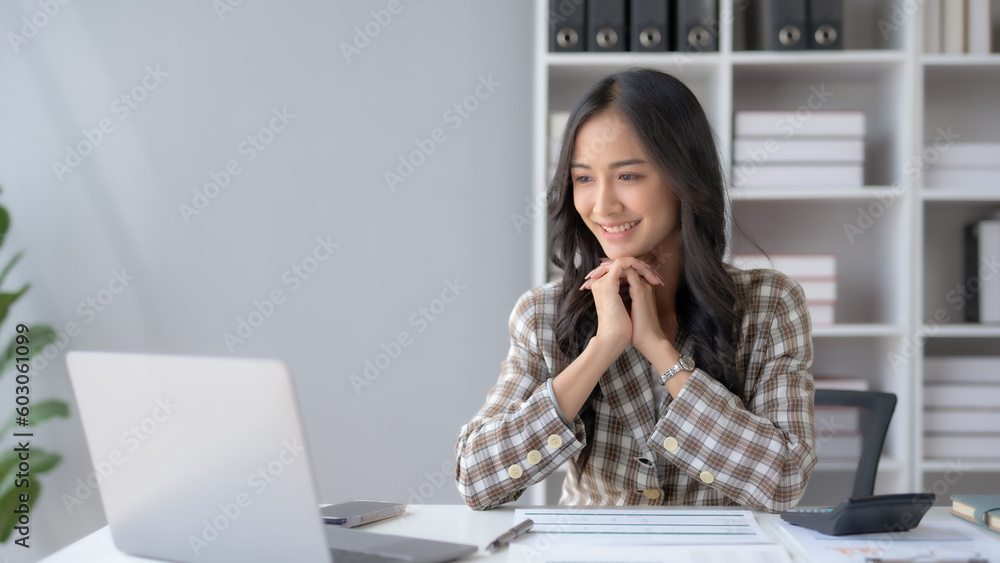 Successful Asian businesswoman smiling using laptop and computer at office. Confident Asia businesswoman sitting happily in the office. Successful Asian businesswoman smiling using laptop and computer at office. Confident Asia businesswoman sitting happily in the office.